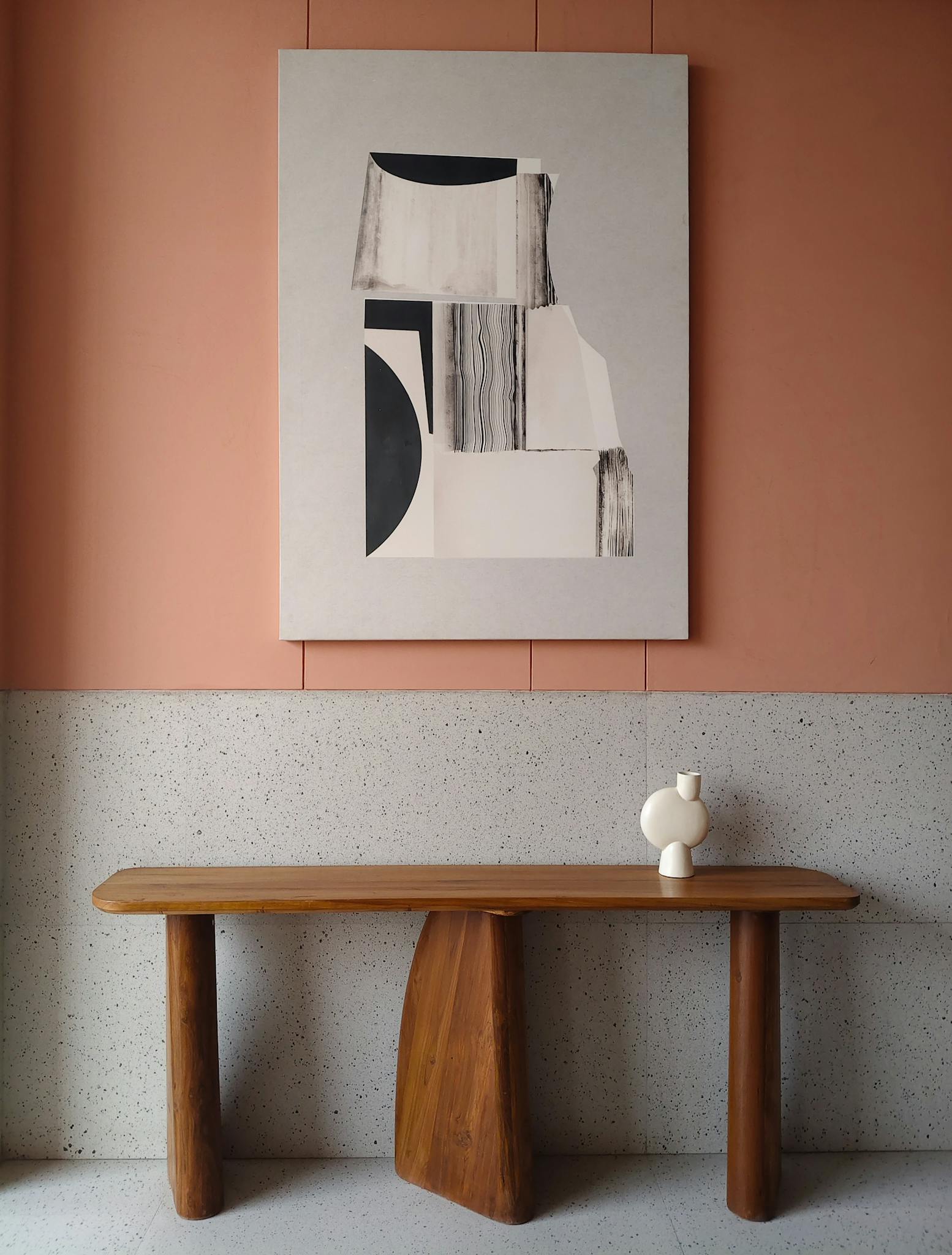 A modern minimalist interior featuring a wooden table and abstract art on a pink textured wall.