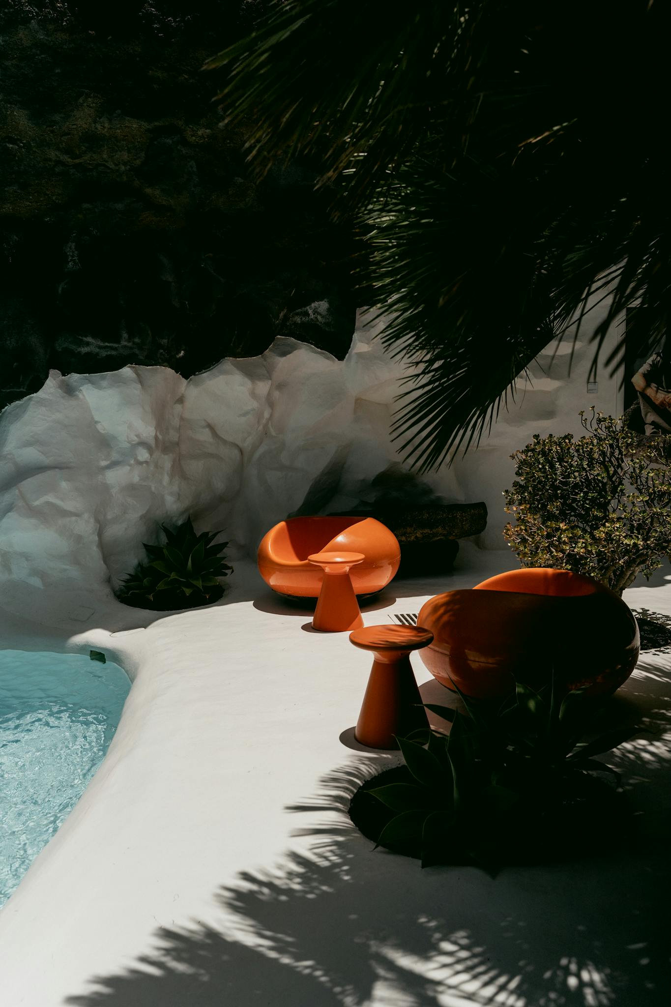 Stylish poolside area with orange chairs under palm shadows, creating a summer escape vibe.